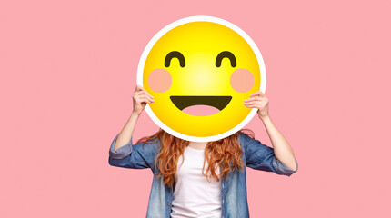 Wall Mural - Redhead girl hiding her face behind happy emoji smile, posing over pink studio background, panorama with copy space