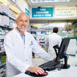 © StarDweller/peopleimages.com - Portrait, mature pharmacist and happy man on computer for healthcare, service or medicine. Pharmacy, face and medical professional in drugstore for stock, sales and online email at checkout counter