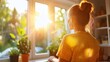 © LifeMedia - A woman gazes out of a sunlit window with various flowering plants on the sill, capturing a serene moment and a sense of peace and contemplation in a home environment.