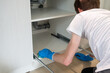 © AnastasiiaAkh - Man cleaning kitchen cabinet with sponge and blue gloves under the sink