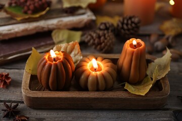 Wall Mural - Burning candles in shape of pumpkins and autumn decor on wooden table