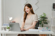 © Wicitr - Focused and Confident: Young Asian Woman Working on Laptop at Home Office Desk.
