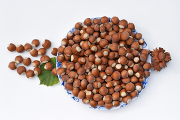 Wall Mural - Hazelnuts in shell on a plate and on a white background with hazel leaf