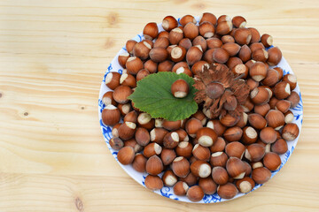 Wall Mural - Hazelnuts in shell with hazel leaf on a plate, wooden background 