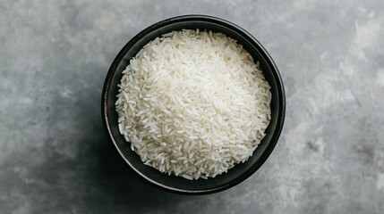 Wall Mural - Simple and elegant top view of white rice in a black bowl against a grey backdrop, focusing on the texture and detail of the rice.