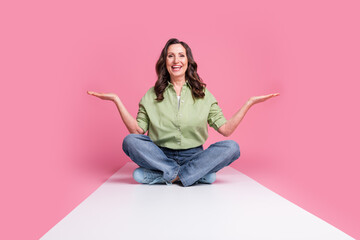 Wall Mural - Photo of grandmother sitting floor podium in jeans and khaki shirt two arms asana meditation isolated on pink color background