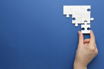 Wall Mural - Woman solving white puzzle on blue background, top view. Space for text