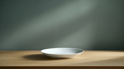 Wall Mural - A simple white plate on a wooden table against a muted green wall, softly lit.