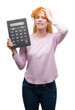 © Krakenimages.com - Young redhead woman holding big calculator stressed with hand on head, shocked with shame and surprise face, angry and frustrated. Fear and upset for mistake.