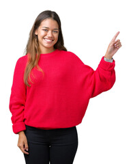 Young beautiful brunette woman wearing red winter sweater over isolated background with a big smile on face, pointing with hand and finger to the side looking at the camera.