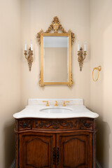 Wall Mural - A bathroom with a dark wood vanity cabinet, white marble countertop, brown walls, and gold faucet, mirror, and sconces.