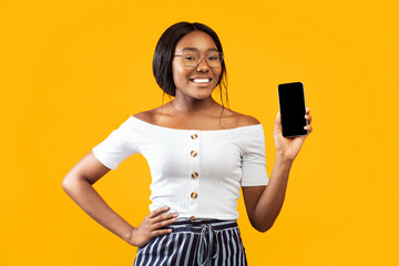 Great App. African American Girl Showing Smartphone Blank Screen Smiling At Camera Standing Over Orange Background. Studio Shot