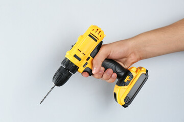 Man with cordless electric drill on light grey background, closeup