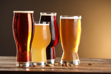 Wall Mural - Glasses with different types of beer and pistachio nuts on wooden table against color background, closeup