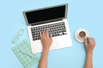 Wall Mural - Female hands with laptop, notebook and cup of coffee on blue background