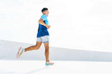 A man in athletic wear runs outdoors under a bright sky, showcasing movement and fitness in an open space.