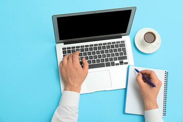 Wall Mural - Male hands with laptop, notebook and cup of coffee on blue background