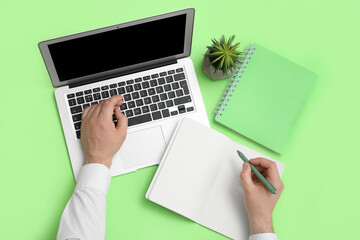 Wall Mural - Male hands with laptop and notebooks on green background