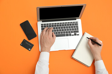 Canvas Print - Male hands with laptop, mobile phone and credit card on orange background