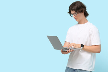 Wall Mural - Male programmer in eyeglasses with laptop on blue background