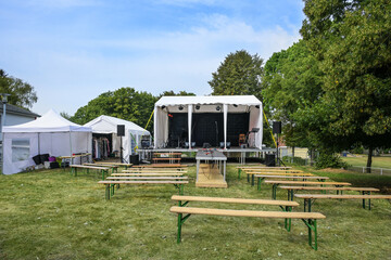 Wall Mural - Open-air stage, tents for technical equipment and as dressing room, wooden benches for the audience, installed on a meadow for a music festival event in the countryside