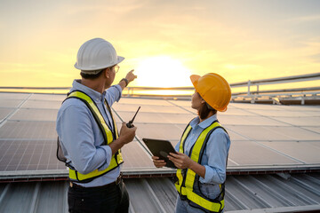 Two people are standing on a roof, one pointing to something on a tablet. Scene is serious and focused, as the two workers are discussing something important