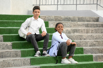 Canvas Print - Group of happy pupils sitting on stairs near school outdoors