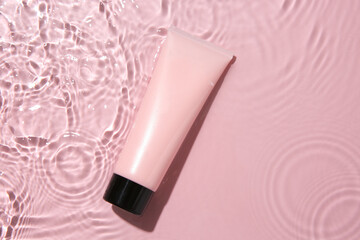 Poster - Cosmetic product. Tube with cream in water on pink background, top view