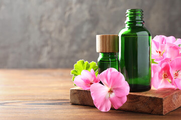 Poster - Geranium essential oil in bottles and beautiful flowers on wooden table, space for text