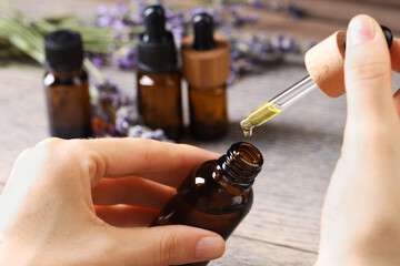 Poster - Woman using essential oil at wooden table, closeup