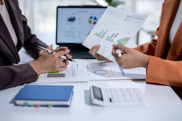 Wall Mural - Businesswomen analyzing financial charts on paper and on a laptop screen, working together in the office