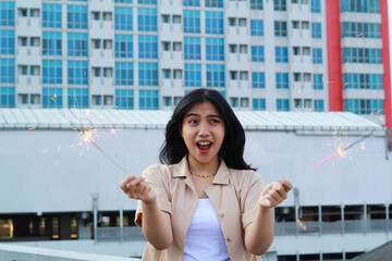 carefree asian young woman holding sparkler celebrate new year eve with laugh and dance in rooftop apartment outdoor with city building background