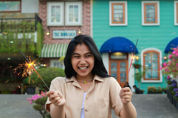 cheerful young asian woman holding sparkler to celebrate new year eve with garden party standing over colorful vintage house yard