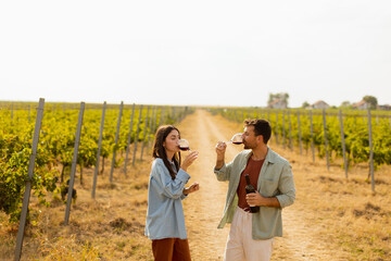 A joyful couple enjoying wine tasting together in a sunny vineyard during the golden hour, surrounded by lush green grapevines