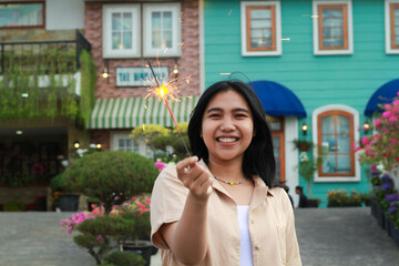 portrait of beautiful happy young asian woman holding sparklers fireworks to celebrate new year eve with garden party standing in outdoor vintage house yard