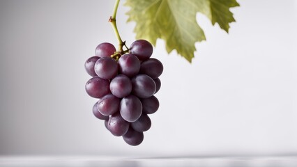 a cluster of purple grapes hanging from a vine leaf against a light background.