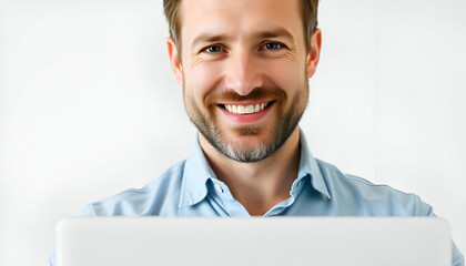 Wall Mural - A smiling young Caucasian man with short brown hair and a beard, working on laptop, wearing a blue denim shirt against a plain white background