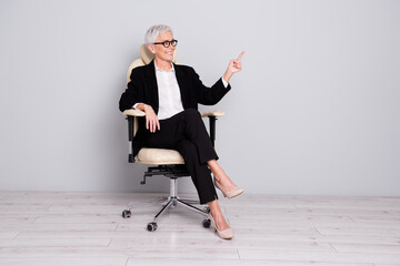 Sticker - Full size photo of pretty senior female entrepreneur sit armchair look point empty space wear formalwear isolated on gray color background