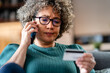 © lordn - A worried woman holds her credit card and speaks on the phone, looking stressed. Her face is expressing concern and frustration.