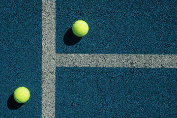 Yellow tennis ball with sunny shadow on blue tennis court with artificial covering. View from above. Sports background.