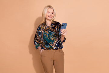 Wall Mural - Photo portrait of blonde hair happy mature business lady in glamour shirt using mobile phone isolated on beige color background