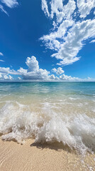 Wall Mural - Crystal clear beach water with gentle waves and bright clouds create serene atmosphere