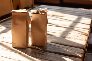 Two paper bags resting on a rustic wooden table illuminated by sunlight in a cozy indoor setting