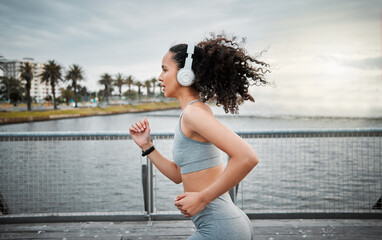 Canvas Print - Woman, headphones and running outdoor for fitness, sports and cardio exercise in morning with music. Female person, listening and jog on bridge for health, training and workout with radio or playlist