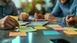 © Your Hand Please - collaborative team working together around a table, hands visible, using sticky notes to brainstorm ideas. The scene emphasizes teamwork, creativity, and problem-solving