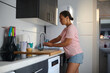 © Taras Grebinets - Woman in casual attire washing dishes in a modern kitchen with stylish utensils and sunlight streaming through the window