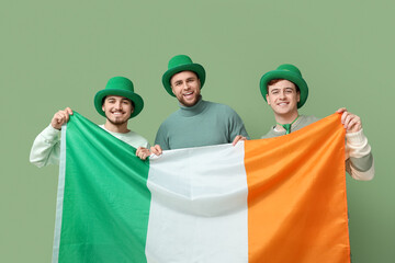 Wall Mural - Happy young men in leprechaun's hats with flag of Ireland on green background. St. Patrick's Day celebration