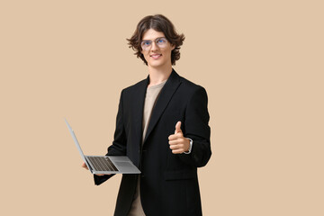 Male programmer in eyeglasses with modern laptop showing thumb-up gesture on beige background