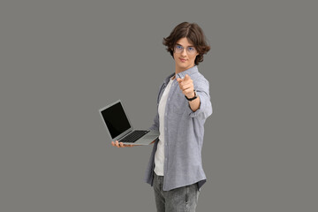 Male programmer in eyeglasses with modern laptop pointing at something on grey background