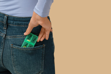 Wall Mural - Young woman with pill organizer in pocket on beige background